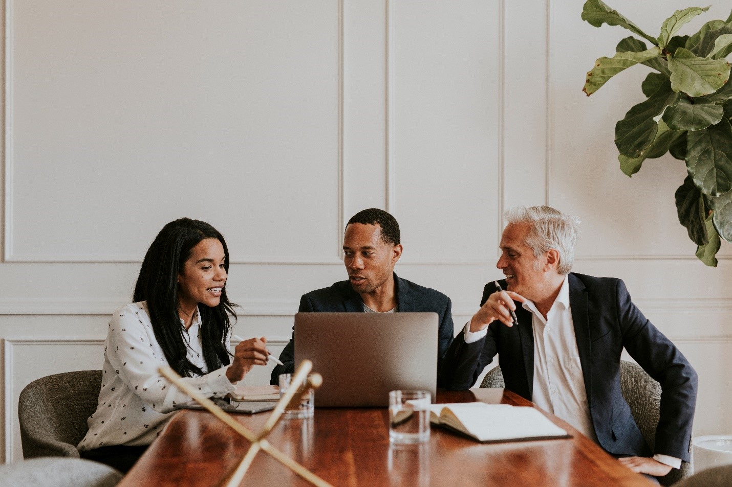 Three professionals sitting at a table around a laptop.