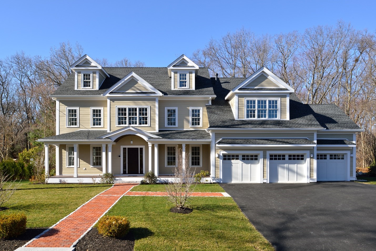 A photograph of a beautiful new construction home The house is two floors plus a dormer and an attached garage. The driveway is paved and there is a decorated walkway that leads to the front door.