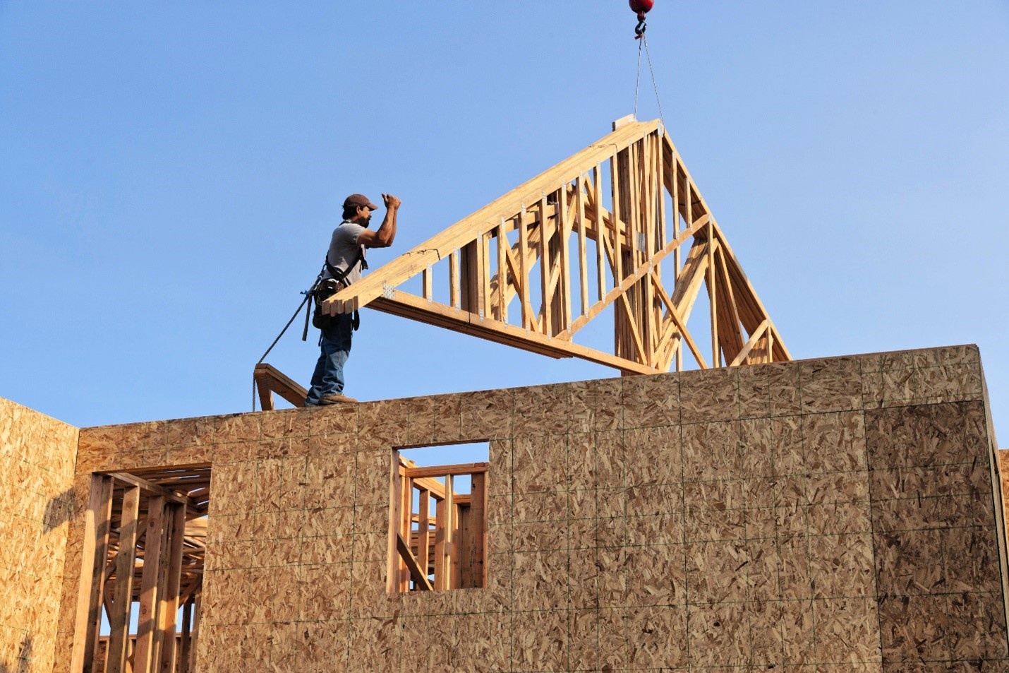 A photograph of a home builder directing a crane where to place a prefabricated roof frame.