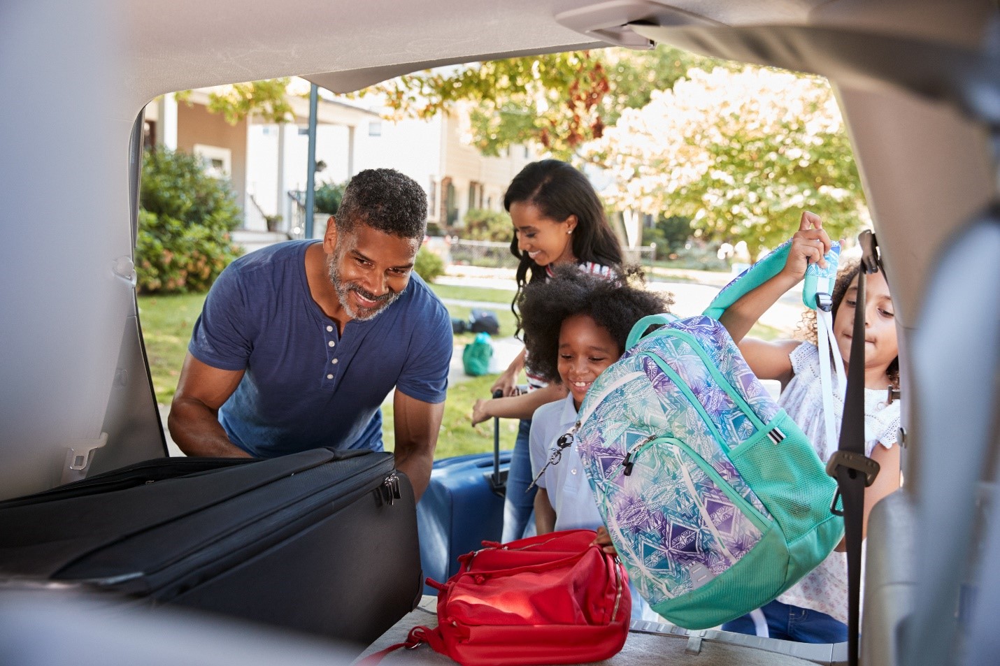 A smiling family packing their suitcases and bags into the back of their car.