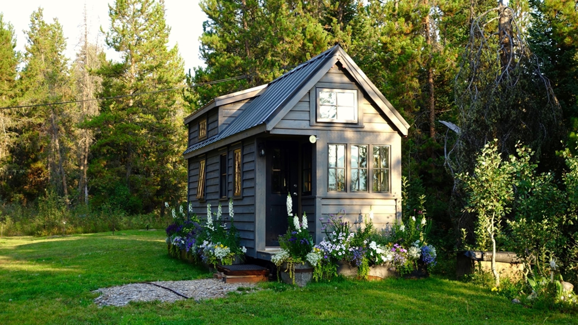 A dark gray tiny home with decorative flowers surrounding it.