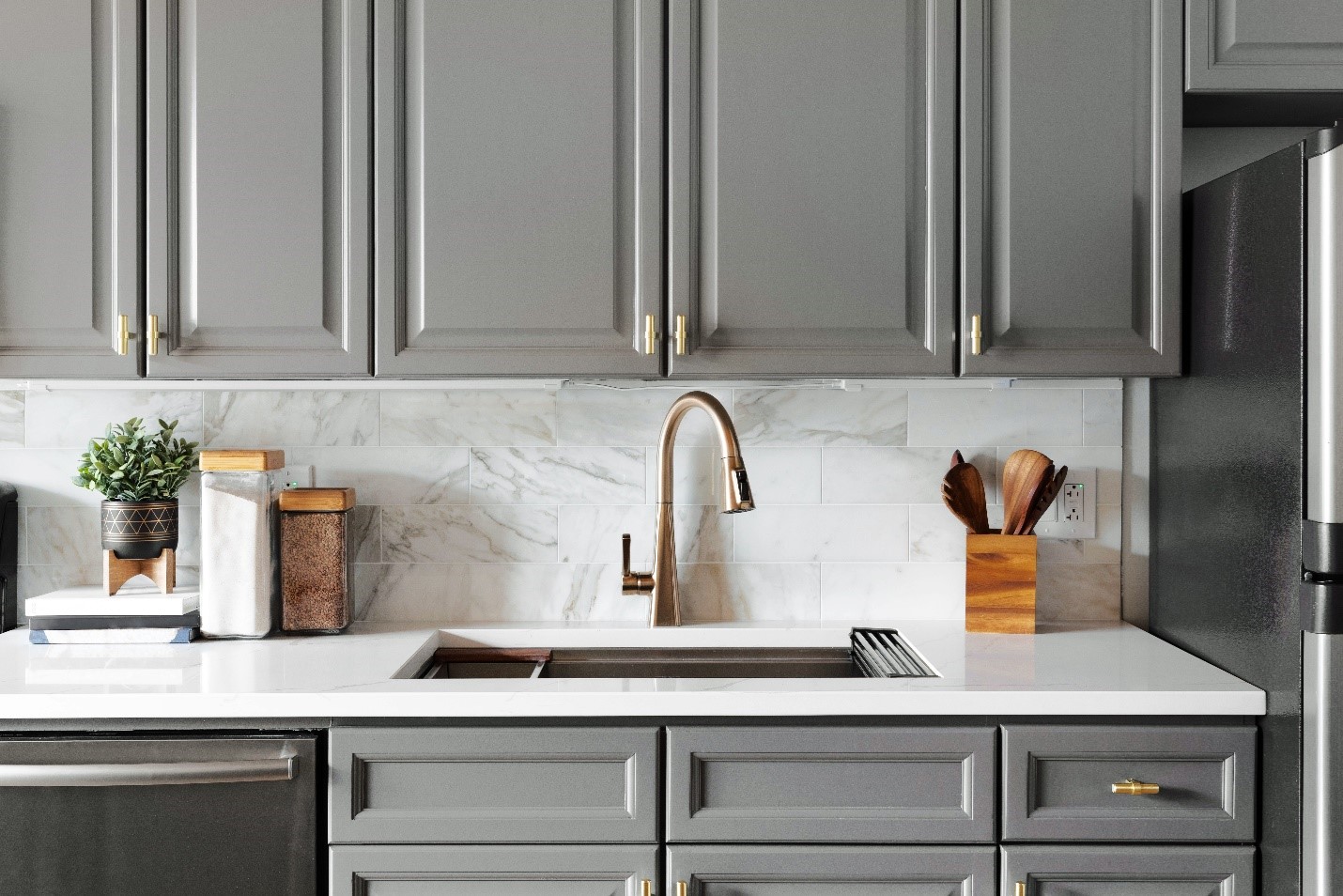 A bronze kitchen sink is visible beneath gray cupboards. Behind the sink is a tiled backsplash reminiscent of white marble.