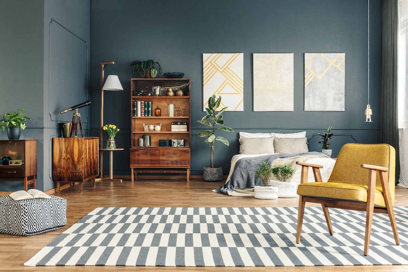 A well-decorated bedroom with cobalt painted walls. There is light filling the space.