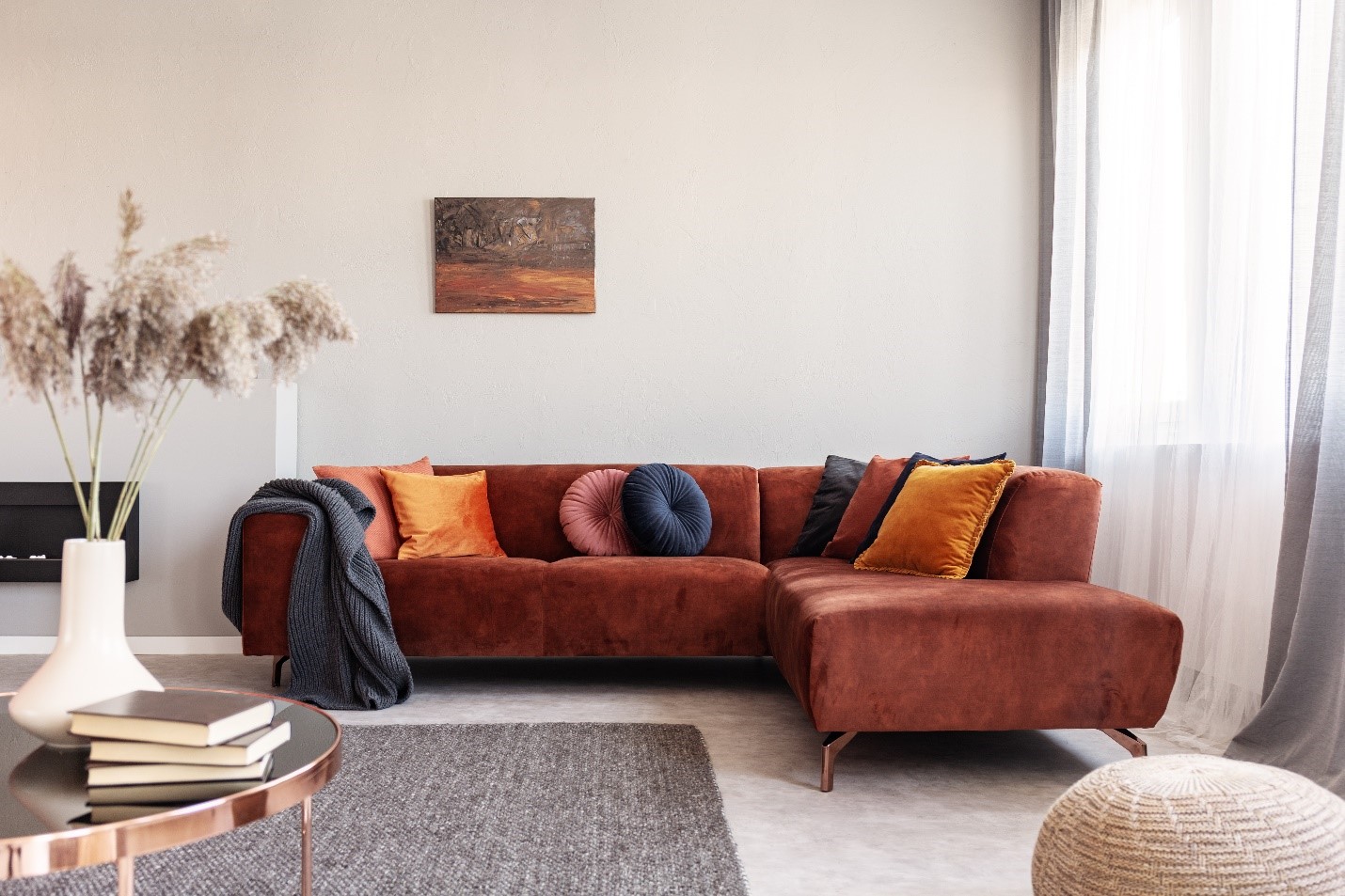 A living room interior featuring a large red-orange couch with velvet crushed pillows in blue, orange, and red.