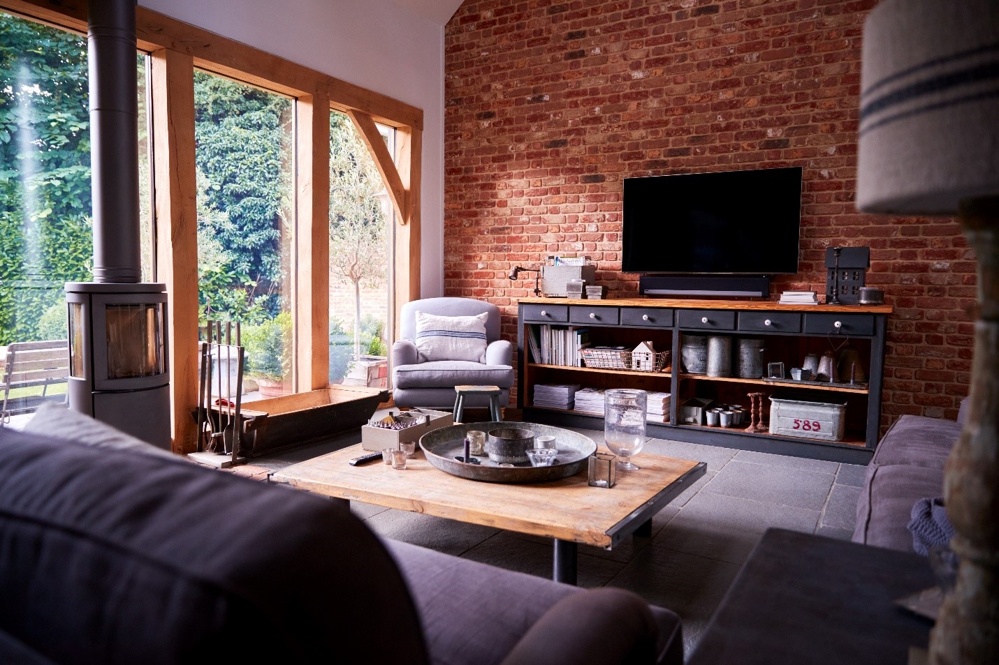 A living space fully decorated with a wood stove, large windows, exposed brick wall, and sitting room.