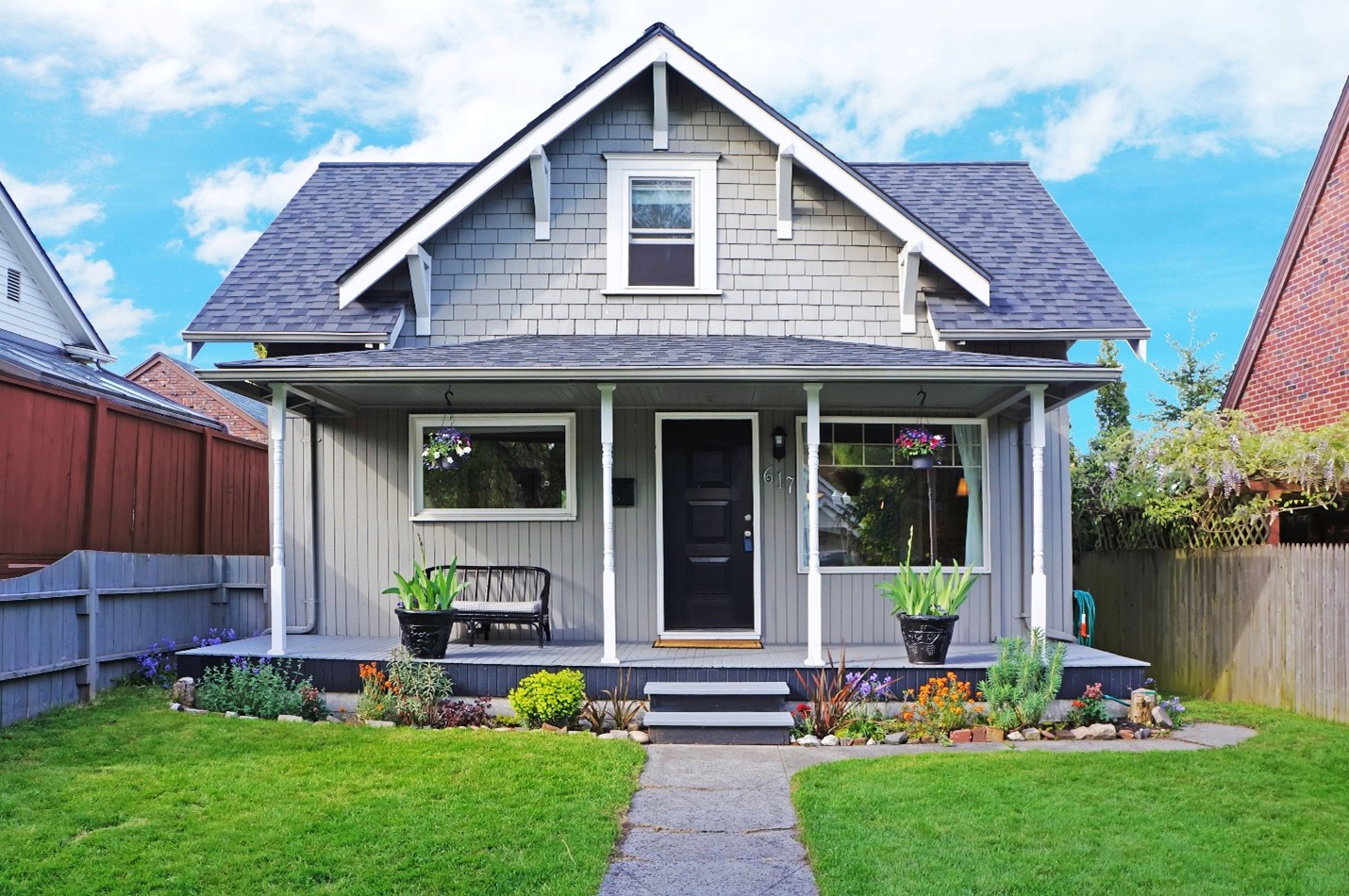 A modest home with beautiful plants in hanging planters, pots, and in the garden.
