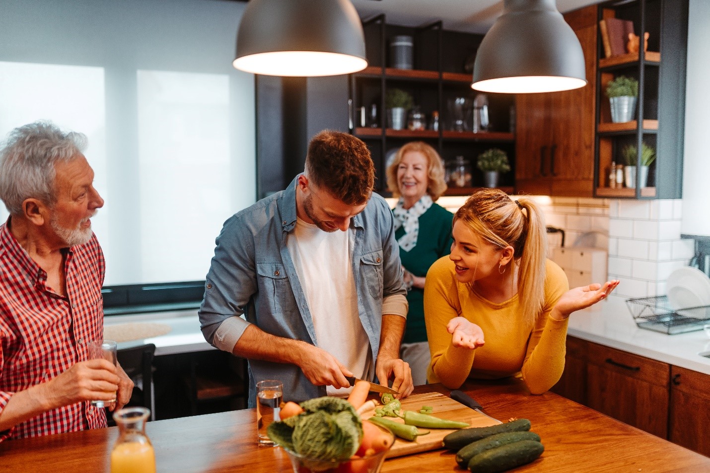 Young adults chatting and laughing in the kitchen with older adults. 