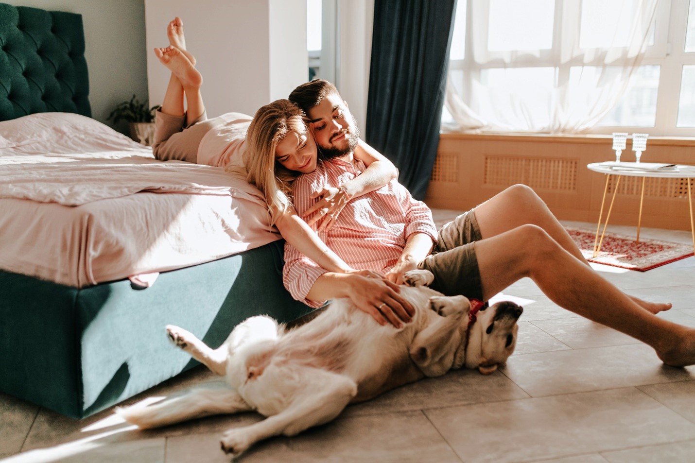 A couple relaxing with their sleepy dog. The dog is upside down and showing their belly as they lean on their owner.