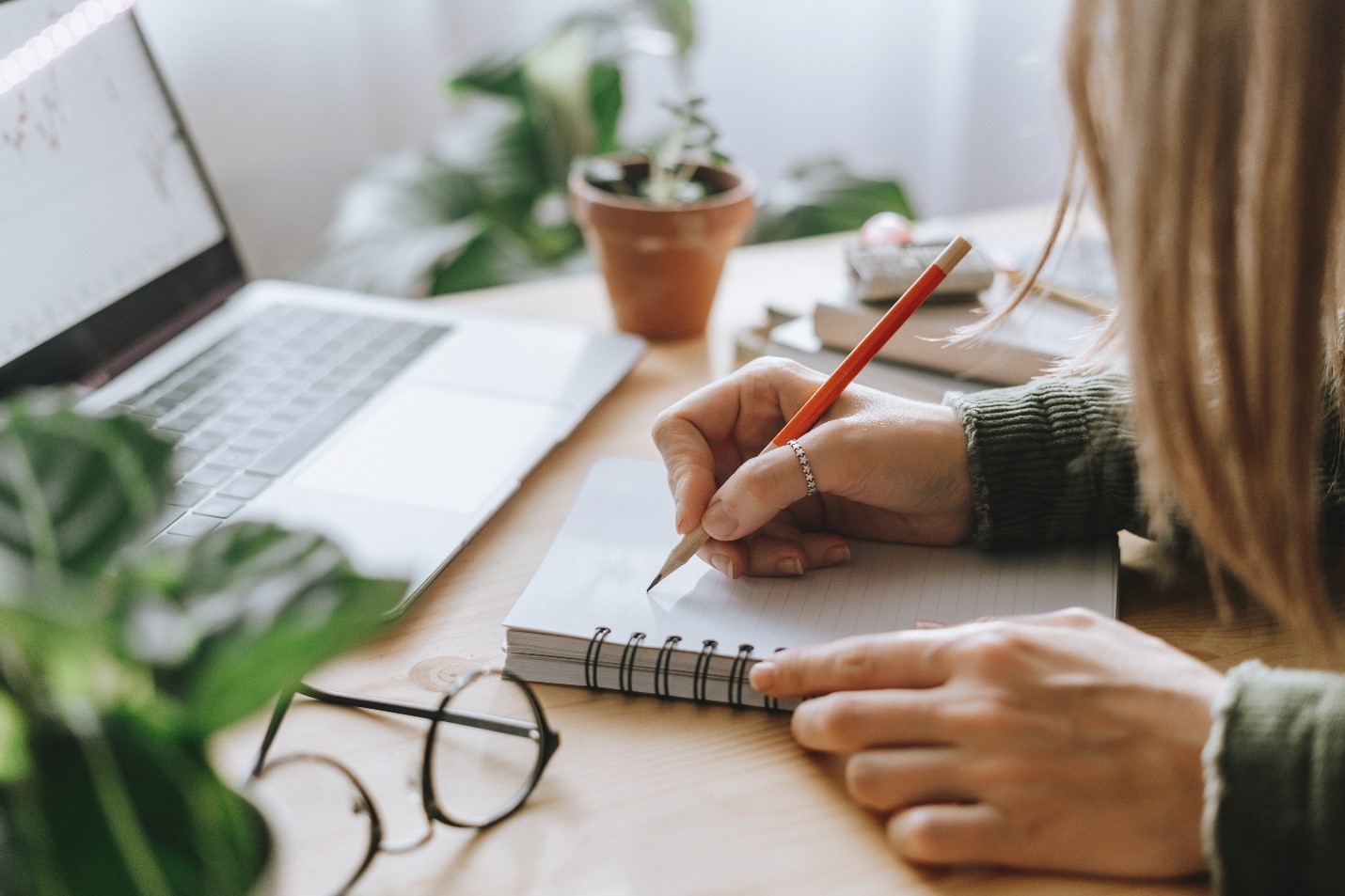 A person with long hair and a thumb ring sketching notes in front of their computer.