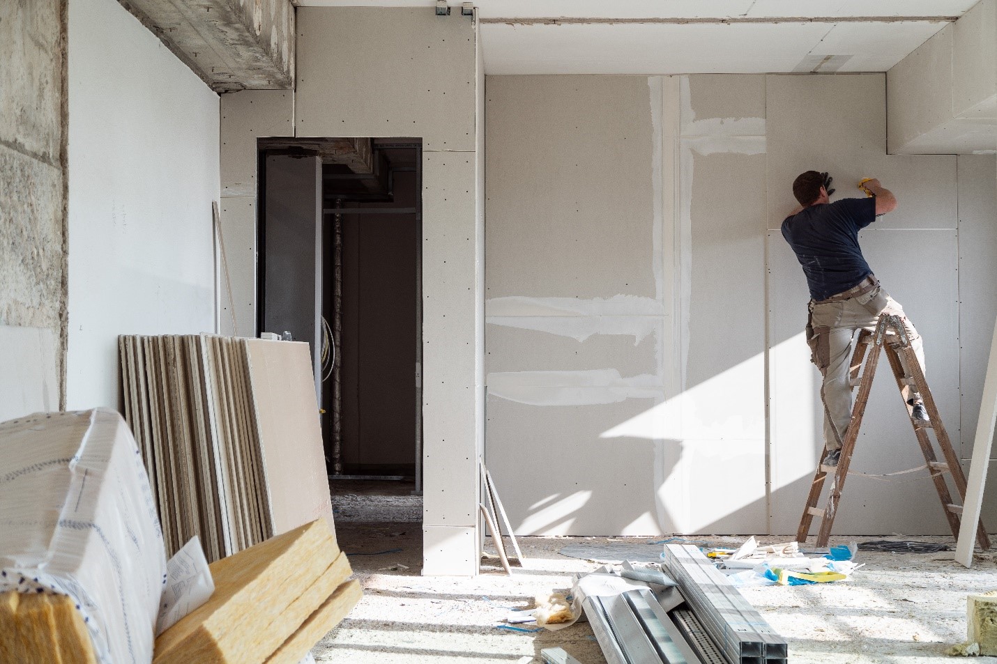 A worker up on a ladder, smoothing out a wall in a construction zone.