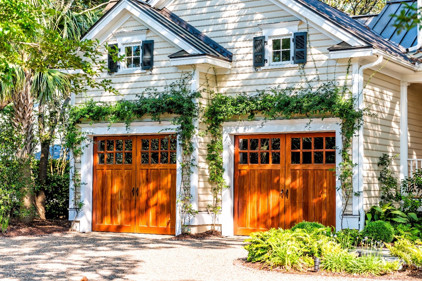 A sunny view of a wooden two door garage with ivy draped over the top.